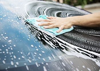 A soapy windshield being cleaned by hand with a microfiber cloth