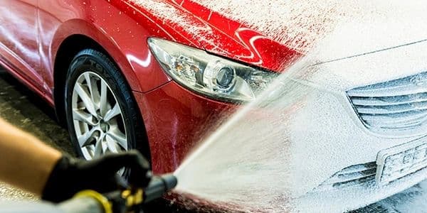 A red car being cleaned with a pressure washer and thick foam