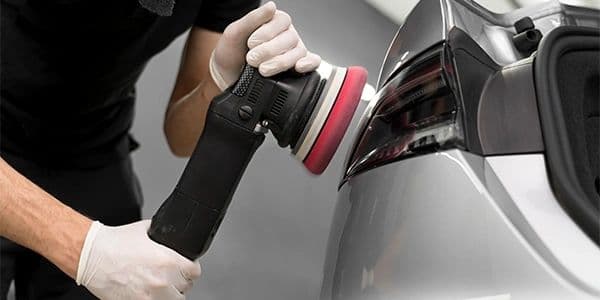 A technician polishing the rear panel of a gray vehicle