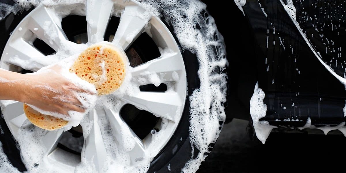 A hand washing a vehicle wheel with a sponge and soap suds